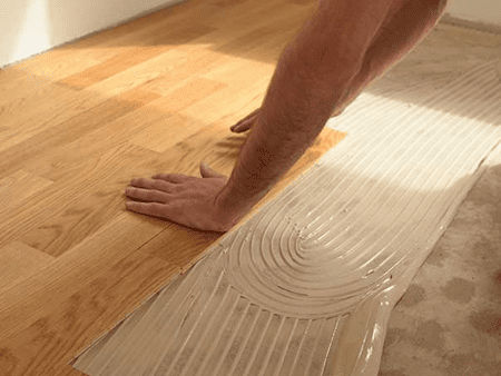 A man installing a hardwood floor in a room.