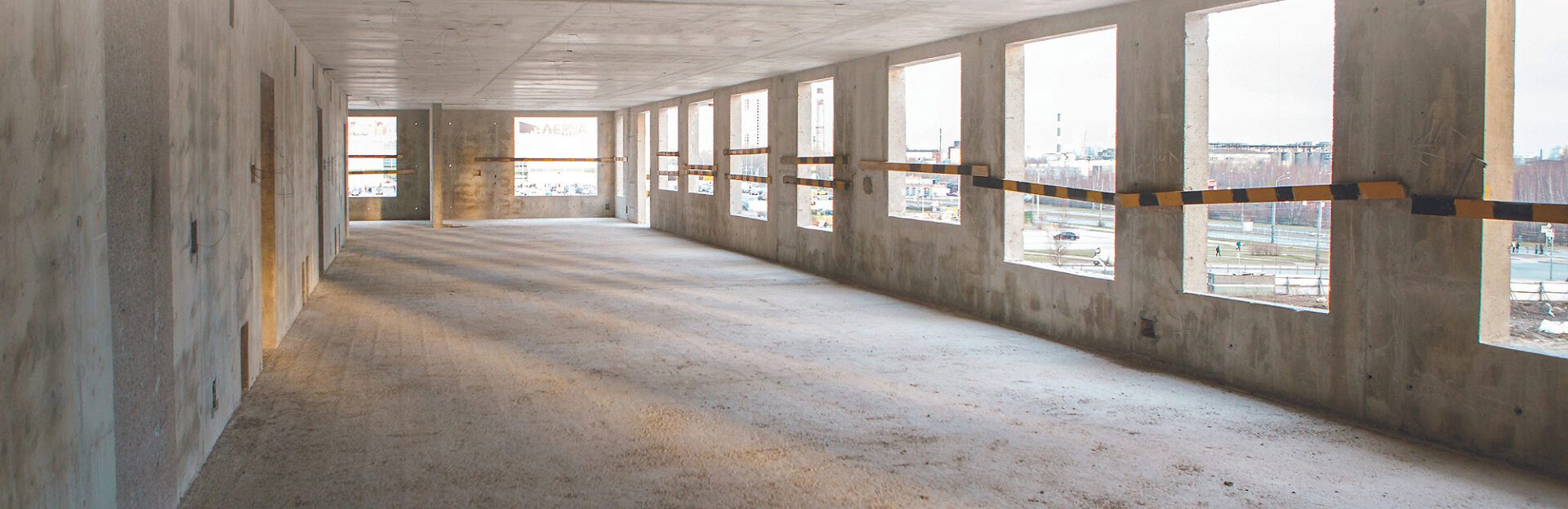 A large empty room with many windows and concrete floors.